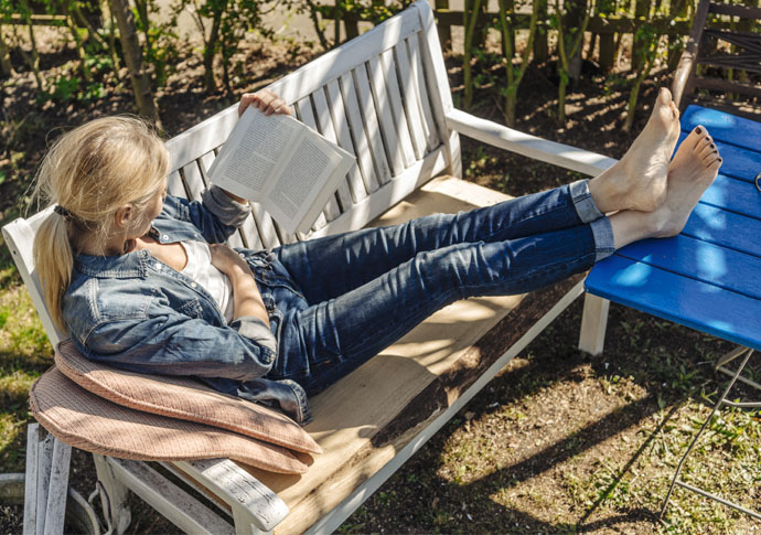 Kvinna läser bok på parkbänk i vårsolen